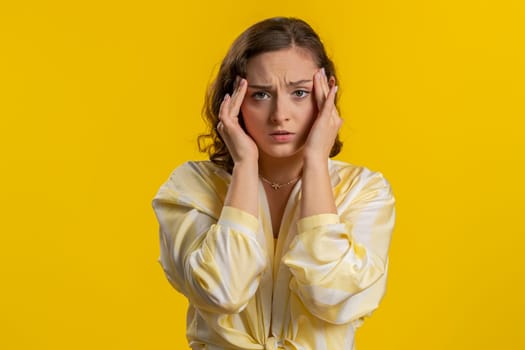 Attractive exhausted young woman girl rubbing temples to cure headache problem, suffering from tension, migaine, stress, grimacing in pain, high blood pressure isolated alone on yellow wall background