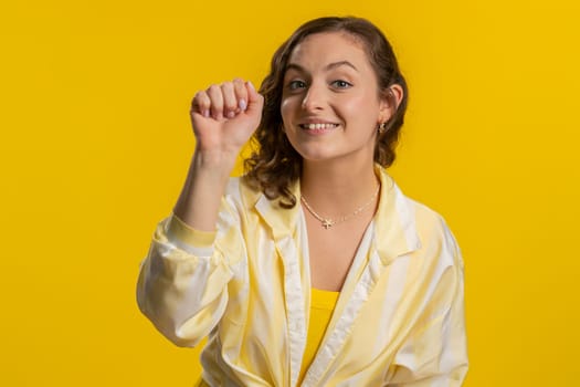 Knock-knock who is there. Excited young woman knocking door gesture asking who is at home, feeling embarrassed, no idea, being clueless and uncertain. Girl isolated alone on studio yellow background