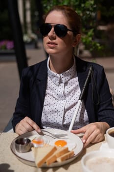 A blind woman in a business suit eats scrambled eggs in a street cafe