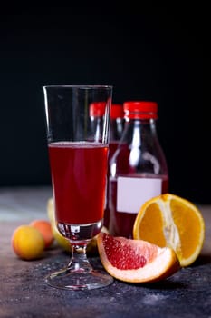 a glass glass with a drink and various fruits on the table.