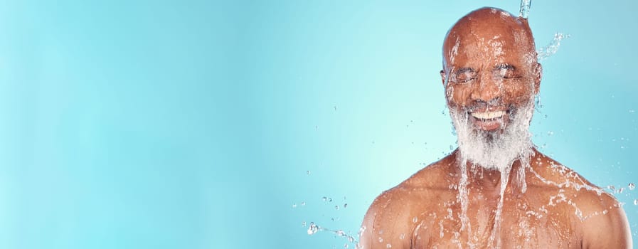Skincare, water splash and senior man in studio for wellness, beauty or skin treatment on blue background. Happy, elderly and guy model smile, cleaning or facial, hygiene and hydration while isolated.