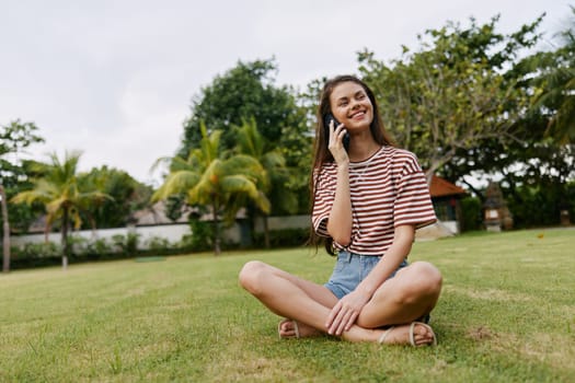 smiling woman call park network phone palm green blogger tree t-shirt mobile human nature girl sitting happy walk smart lifestyle talk grass