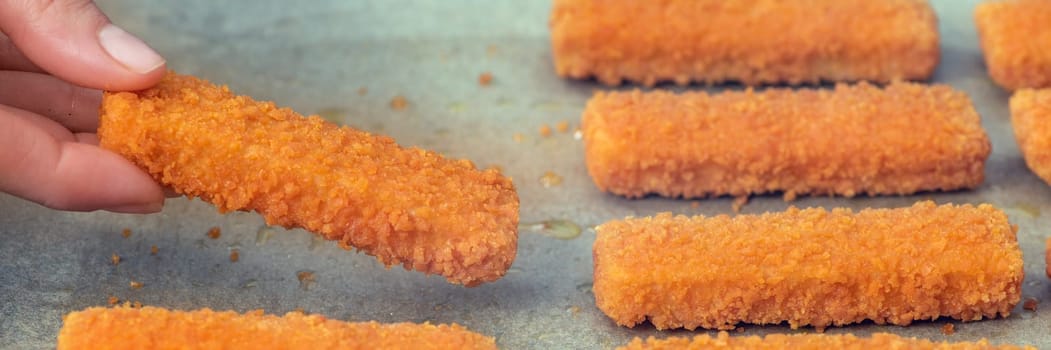 The hand lays out the fish fingers on the frying paper. The concept of frying fish sticks in the oven. Side view. Close-up. High quality photo