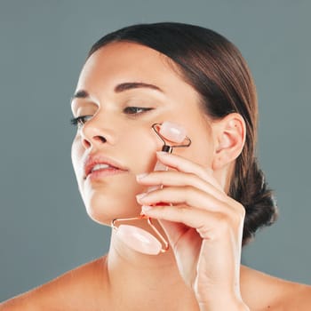 Face massage closeup with roller, woman and skincare, beauty and healthy skin isolated on studio background. Natural cosmetics, glow and rose quartz makeup tools in hand, manicure and cosmetic care.