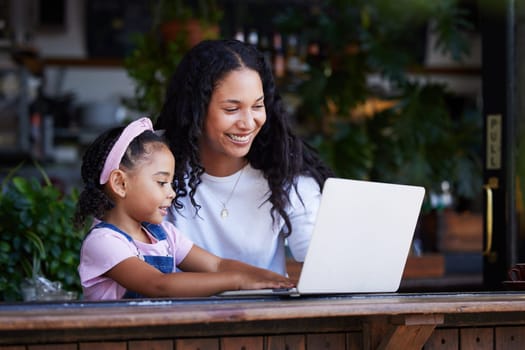 Mother, learning and girl with laptop at cafe for education and development online. Family, remote worker and happy woman teaching kid how to type on computer at restaurant, bonding and having fun