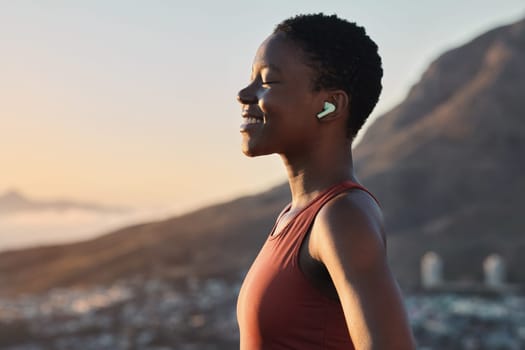 Headphones, fitness or zen black woman on a mountain for peaceful, calm and breathing in relaxing fresh air. Breathe, healthy or happy sports athlete with smile streaming radio music, song or podcast.