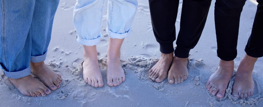 Beach feet, friends and people on vacation, holiday or summer trip. Toes, freedom and group of men and women standing on sandy seashore, seaside or coast, having fun or enjoying quality time outdoors.