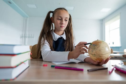 Caucasian schoolgirl sits at her desk at school and studies the globe