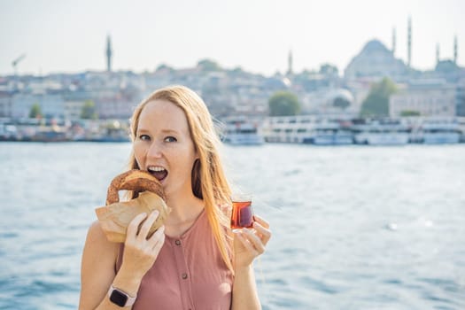 Woman in Istanbul having breakfast with Simit and a glass of Turkish tea. Glass of Turkish tea and bagel Simit against golden horn bay in Istanbul, Turkey. Turkiye.