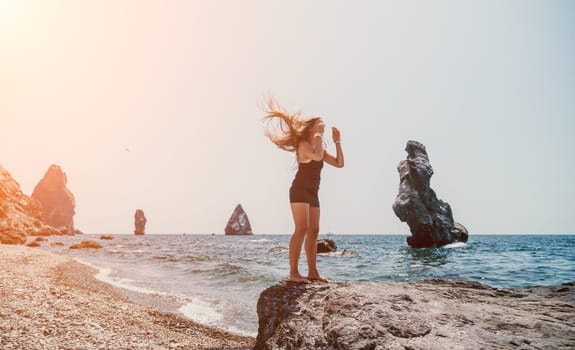 Woman travel sea. Young Happy woman in a long red dress posing on a beach near the sea on background of volcanic rocks, like in Iceland, sharing travel adventure journey