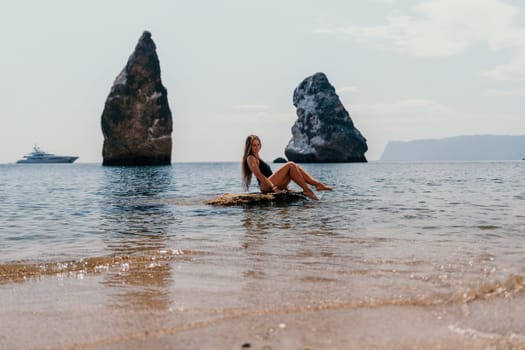 Woman travel sea. Young Happy woman in a long red dress posing on a beach near the sea on background of volcanic rocks, like in Iceland, sharing travel adventure journey