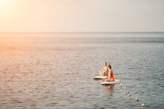 Woman sup yoga. Middle age sporty woman practising yoga pilates on paddle sup surfboard. Female stretching doing workout on sea water. Modern individual hipster outdoor summer sport activity