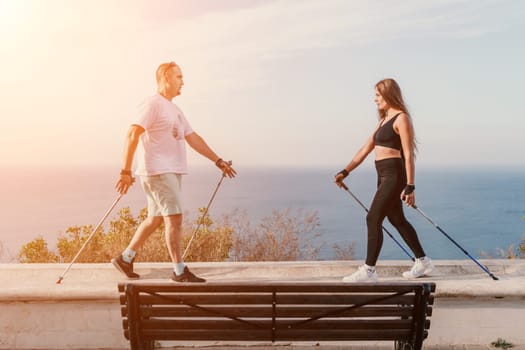 Happy Middle aged couple or friends practicing nordic walking in park near sea. Mature couple with trekking poles walking, practicing Nordic walking outdoors. Aging youthfully and sport concept.