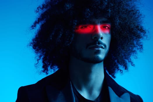 Fashion portrait of a man with curly hair on a blue background with a red stripe of light, multicolored light, trendy, modern concept. High quality photo