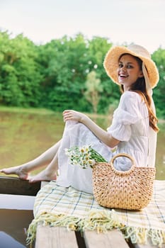 portrait of a cute woman in a hat sitting on a plaid at the pier by the lake. High quality photo