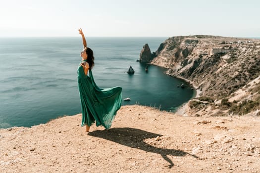 Woman green dress sea. Female dancer posing on a rocky outcrop high above the sea. Girl on the nature on blue sky background. Fashion photo