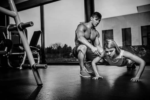 Sportive woman doing plank exercise training back and press muscles with trainer. Sport fitness workout strength power concept. Work in the gym. Black and white
