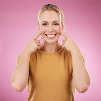 Teeth whitening, portrait and pointing woman in studio, pink background and backdrop. Happy female model, mouth and smile for dental wellness, tooth implant and aesthetic facial of beauty cosmetics.