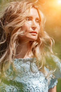 Portrait of a blonde in the park. Happy woman with long blond hair in a blue dress