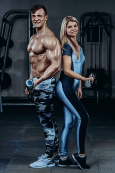 Fitness couple - woman and man with dumbbells in gym. Personal trainer with a gorgeous body without a T-shirt with young woman