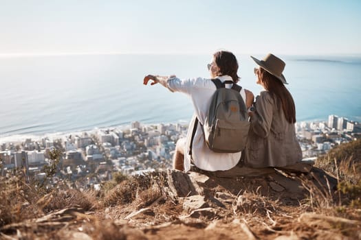 Pointing, view and couple on a mountain for hiking, travel and trekking in Switzerland. Relax, adventure and man and woman sitting on a cliff looking at the city from nature while on vacation.