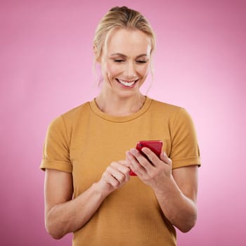 Woman, phone and typing online for communication, social media and chat on pink background. Happy mature model with smartphone in hands for network connection or writing post on mobile app website.