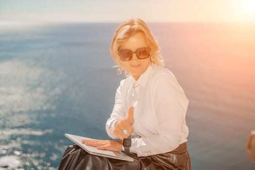 Business woman on nature in white shirt and black skirt. She works with an iPad in the open air with a beautiful view of the sea. The concept of remote work