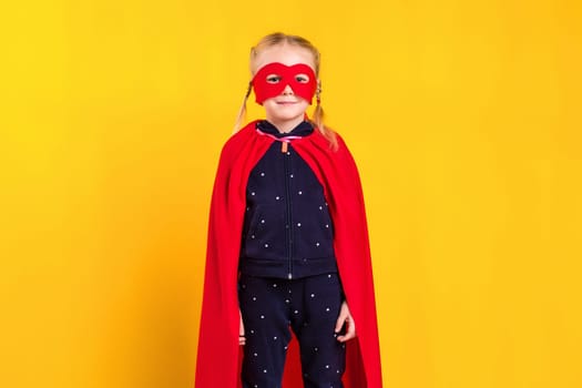 Superhero little girl in a red raincoat and a mask on a yellow background. Studio photography