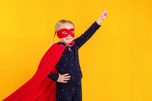 Superhero little girl in a red raincoat and a mask on a yellow background. Studio photography