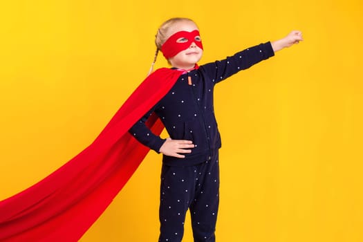 Superhero little girl in a red raincoat and a mask on a yellow background. Studio photography