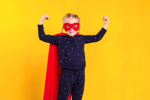 Superhero little girl in a red raincoat and a mask on a yellow background. Studio photography