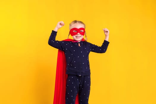 Superhero little girl in a red raincoat and a mask on a yellow background. Studio photography