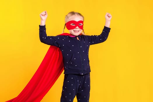 Superhero little girl in a red raincoat and a mask on a yellow background. Studio photography