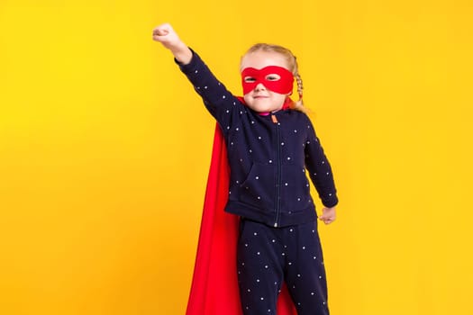 Superhero little girl in a red raincoat and a mask on a yellow background. Studio photography