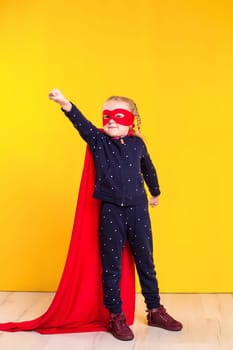 Superhero little girl in a red raincoat and a mask on a yellow background. Studio photography