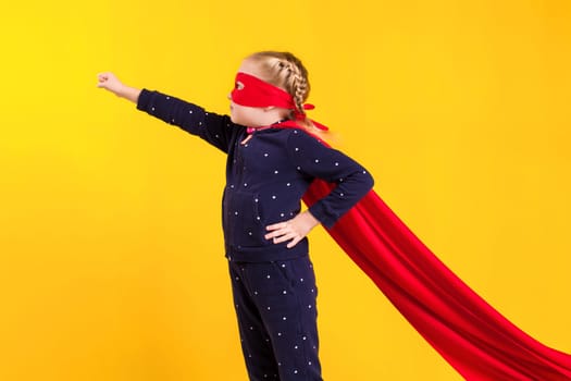 Superhero little girl in a red raincoat and a mask on a yellow background. Studio photography