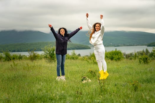 Two girls with long hair are jumping in a clearing overlooking the mountains. The concept of travel and tourism to different countries