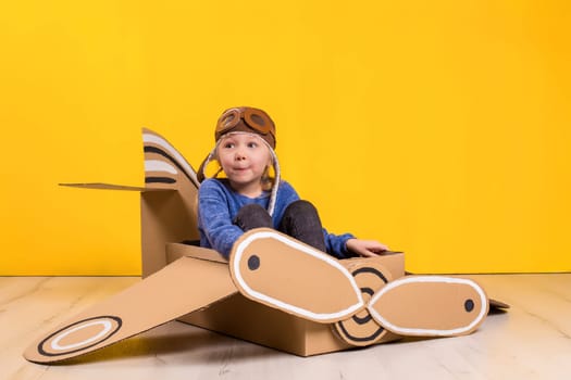 Little dreamer girl playing with a cardboard airplane. Childhood. Fantasy, imagination. Studio photography on a yellow background. Imagination or exploration concept
