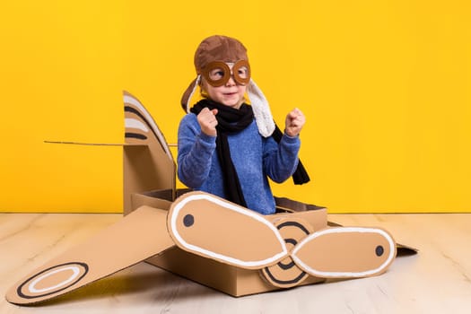Little dreamer girl playing with a cardboard airplane. Childhood. Fantasy, imagination. Studio photography on a yellow background. Imagination or exploration concept