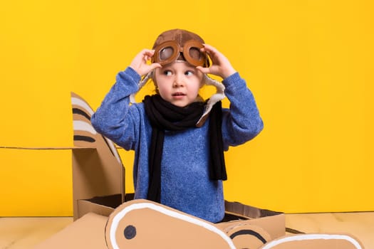 Little dreamer girl playing with a cardboard airplane. Childhood. Fantasy, imagination. Studio photography on a yellow background. Imagination or exploration concept