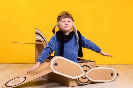 Little dreamer girl playing with a cardboard airplane. Childhood. Fantasy, imagination. Studio photography on a yellow background. Imagination or exploration concept