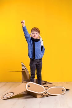 Little dreamer girl playing with a cardboard airplane. Childhood. Fantasy, imagination. Studio photography on a yellow background. Imagination or exploration concept