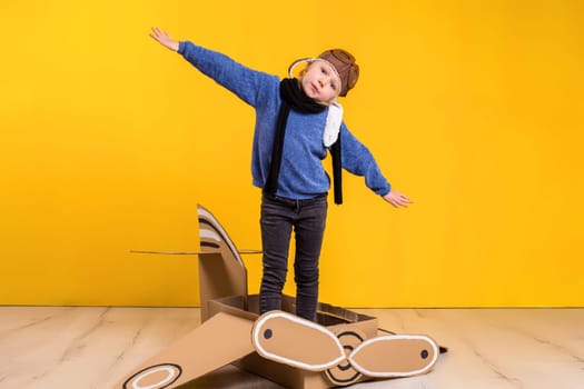 Little dreamer girl playing with a cardboard airplane. Childhood. Fantasy, imagination. Studio photography on a yellow background. Imagination or exploration concept