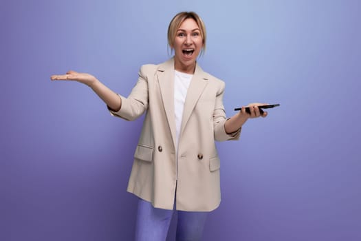 blonde young woman in a jacket makes a payment using a phone on a studio background.