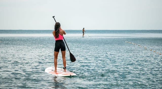 Sea woman and man on sup. Silhouette of happy young woman and man, surfing on SUP board, confident paddling through water surface. Idyllic sunset. Active lifestyle at sea or river