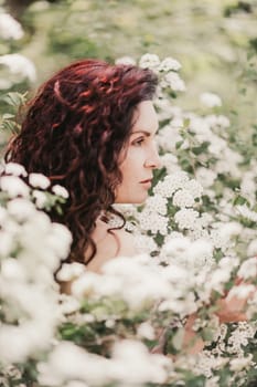 Woman spirea flowers. Portrait of a curly happy woman in a flowering bush with white spirea flowers