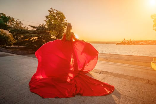 Sunrise red dress. A woman in a long red dress against the backdrop of sunrise, bright golden light of the sun's rays. The concept of femininity, harmony