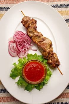 Grilled pork kebab with red onion and chilly souce on a white plate