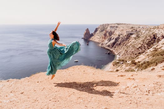 Woman green dress sea. Female dancer posing on a rocky outcrop high above the sea. Girl on the nature on blue sky background. Fashion photo