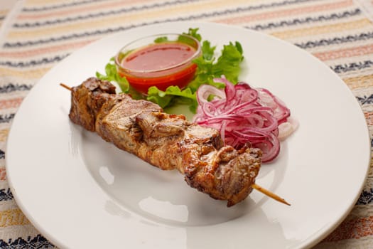 Grilled pork kebab with red onion and chilly souce on a white plate